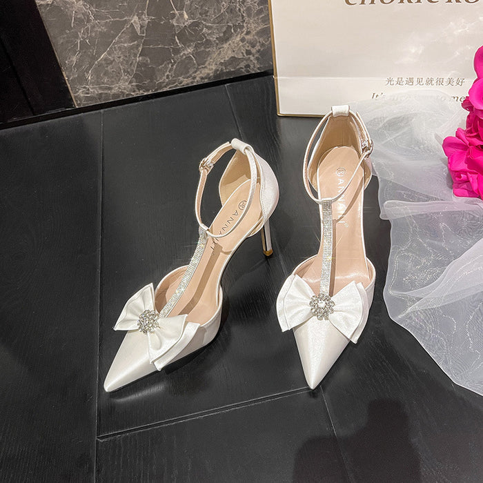 White high-heeled shoes with decorative bows on a dark surface