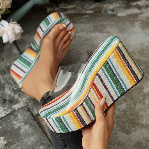 Colorful striped shoes with clear heel being held by a person on a concrete surface.