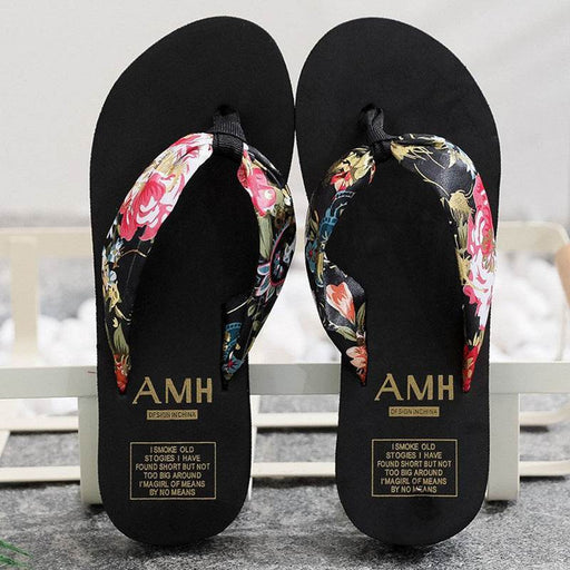 Black flip-flops with floral straps and 'AMH' branding on a light background
