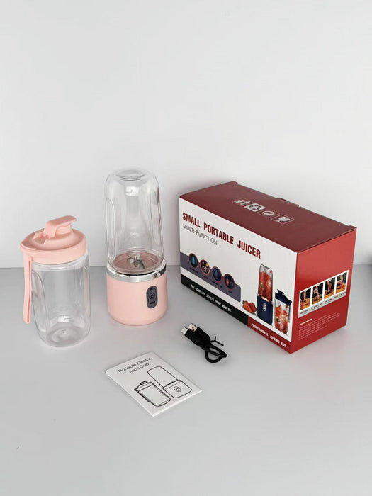 Pink portable juicer with clear container, packaging, and USB cable on a white background
