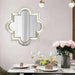 Decorative wall mirror above a dining table with wine glasses and flowers.