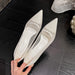 Pair of silver high-heeled shoes held by a hand on a dark wooden floor.