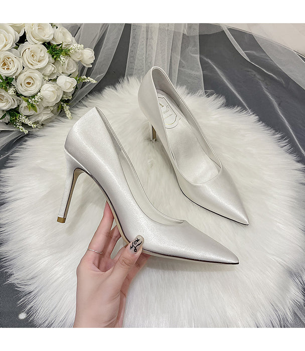 Silver high-heeled shoes on a white fur surface with a bouquet of white flowers in the background.