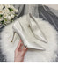Silver high-heeled shoes on a white fur surface with a bouquet of white flowers in the background.