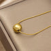 A gold ball pendant necklace on a delicate gold snake chain, displayed on a textured beige jewelry box.