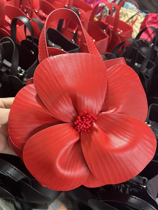 Red floral-shaped handbag held by a person with more bags in the background.