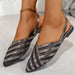 Black and silver strappy shoes worn by a person on a light background