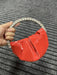 Red handbag with a decorative headband held by a hand on a textured gray background