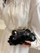 A person in a white blouse holds a black sequined clutch bag with a gold-tone frame and chain strap.