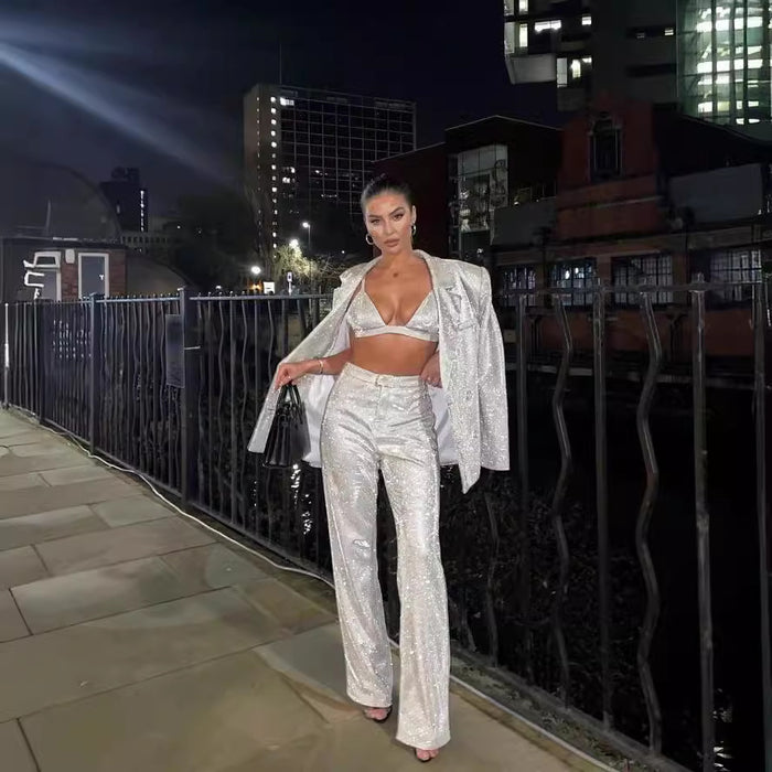 Woman in a sparkling outfit standing on a rooftop at night with cityscape in the background
