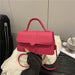 A bright pink structured handbag with a top handle and thin shoulder strap, held by a hand over a white textured blanket in an indoor setting.