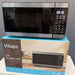 A Vitaps 20L microwave oven with a stainless steel and black glass door, shown resting on top of its blue and brown retail packaging box.