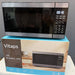 A Vitaps 20L microwave oven with a stainless steel and black glass door, shown resting on top of its blue and brown retail packaging box.