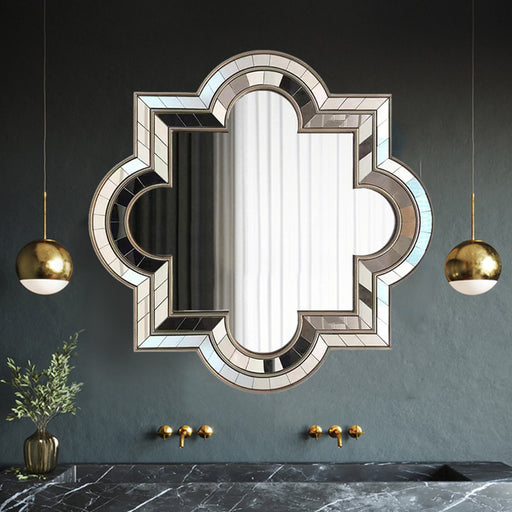Decorative mirror with geometric frame on a dark wall with gold pendant lights.