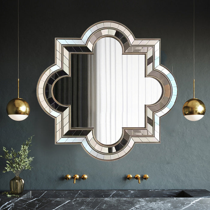 Decorative mirror with geometric frame on a dark wall with gold pendant lights.