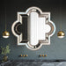 Decorative mirror with geometric frame on a dark wall with gold pendant lights.