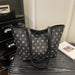 A black tote bag with a repeating white geometric monogram pattern, resting on a dark textured surface next to a black cabinet and a white book.