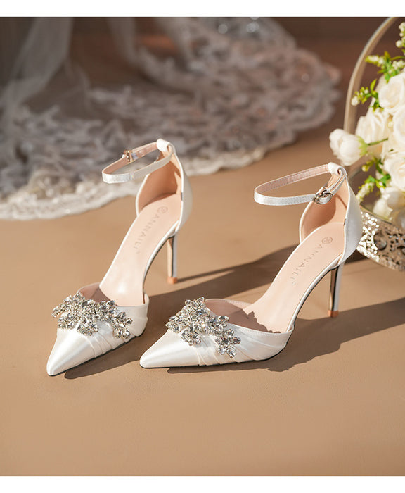 White high-heeled shoes with decorative embellishments on a beige surface.