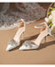 White high-heeled shoes with decorative embellishments on a beige surface.