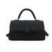 A black structured handbag with a top handle, a front flap, and a small gold-tone buckle detail on the side, shown against a plain white background.