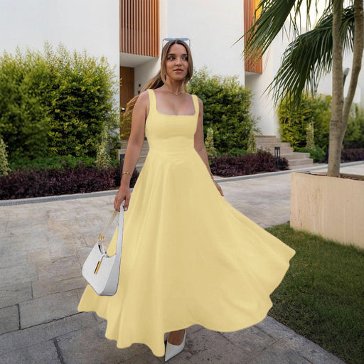 Woman in a yellow dress standing outdoors with greenery and a building in the background