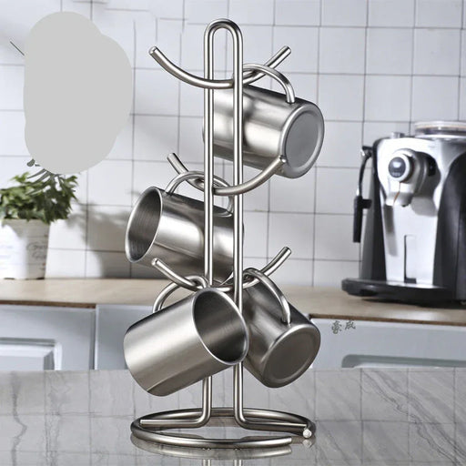 Metal mug rack holding four stainless steel mugs on a kitchen counter with a coffee machine in the background.