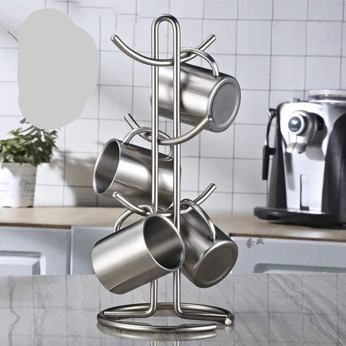 Metal mug rack holding four stainless steel mugs on a kitchen counter with a coffee machine in the background.