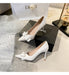 White high-heeled shoes with bow details on a surface with Dior and Chanel boxes in the background.