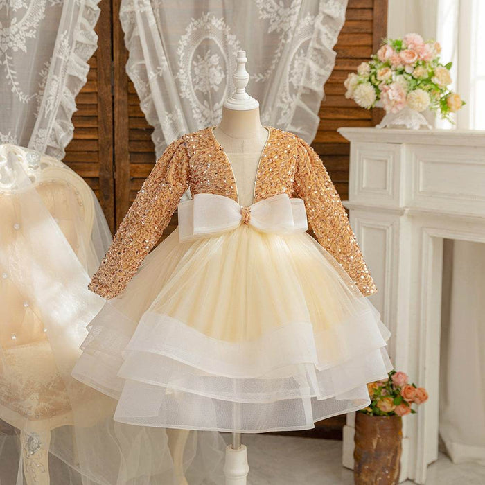 Children's dress with gold sequin top and white tulle skirt on a mannequin against a decorative background.
