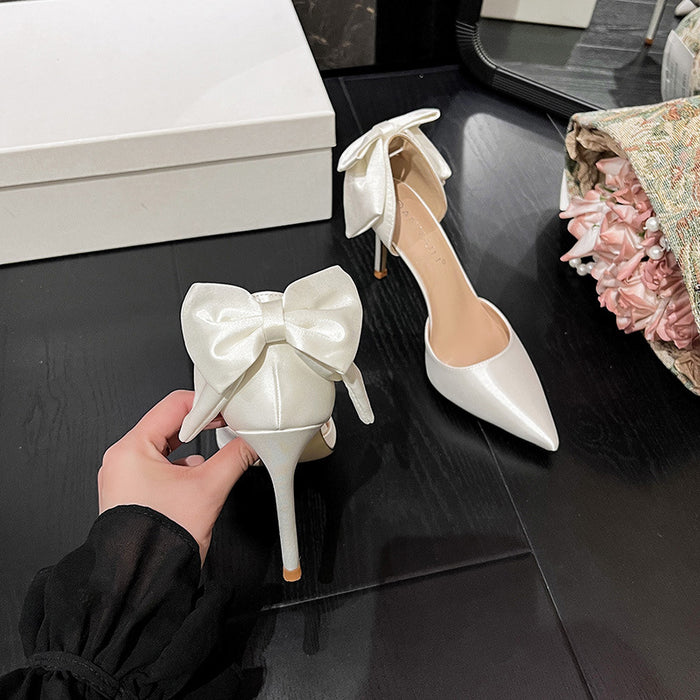White high-heeled shoes with bow details on a dark surface.