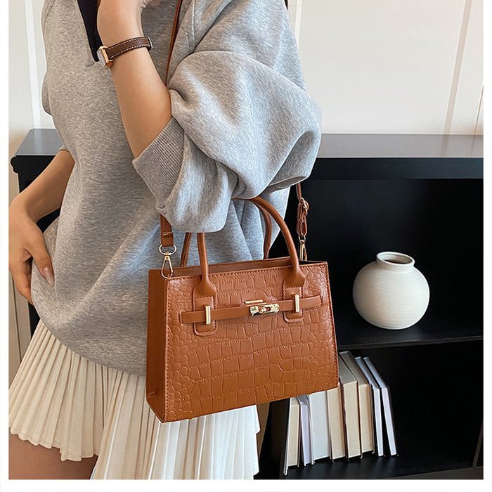 A woman wearing a gray sweatshirt and pleated white skirt carries a brown crocodile-embossed leather handbag with gold-tone hardware in a modern indoor setting.