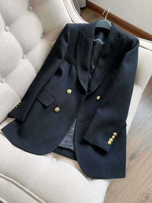 A black double-breasted blazer with gold buttons, displayed on a hanger over a cream tufted armchair.