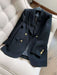 A black double-breasted blazer with gold buttons, displayed on a hanger over a cream tufted armchair.