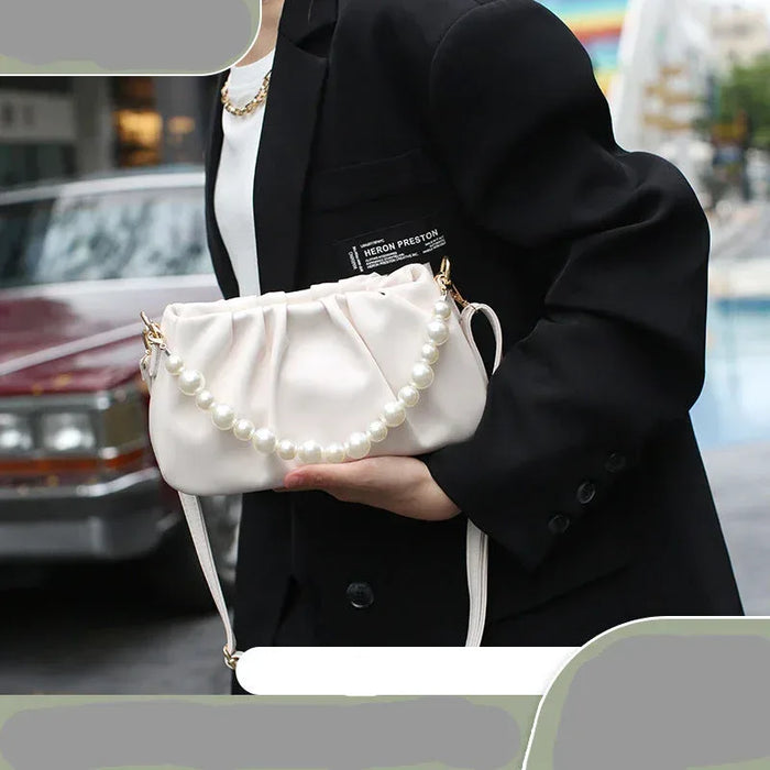 Person holding a white handbag with pearl details in an urban setting