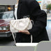 Person holding a white handbag with pearl details in an urban setting
