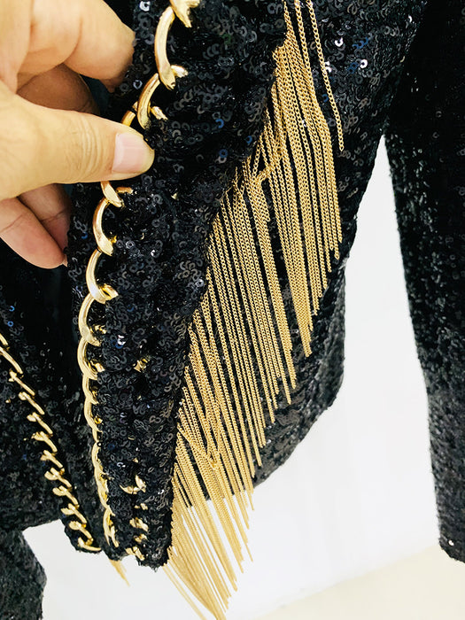 Black textured bag with gold chains and fringes held by a hand on a white background