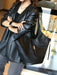 Person wearing a black leather jacket holding a large black handbag indoors.