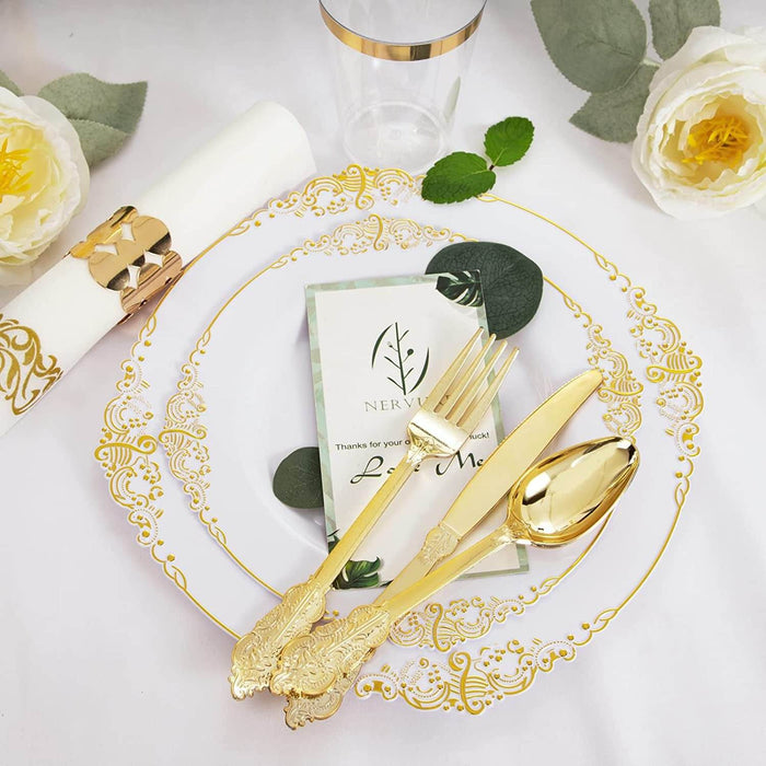 Decorative table setting with gold cutlery, ornate plate, and white roses on a white background.