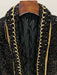 Black sequined garment with gold trim on a wooden hanger against a neutral background