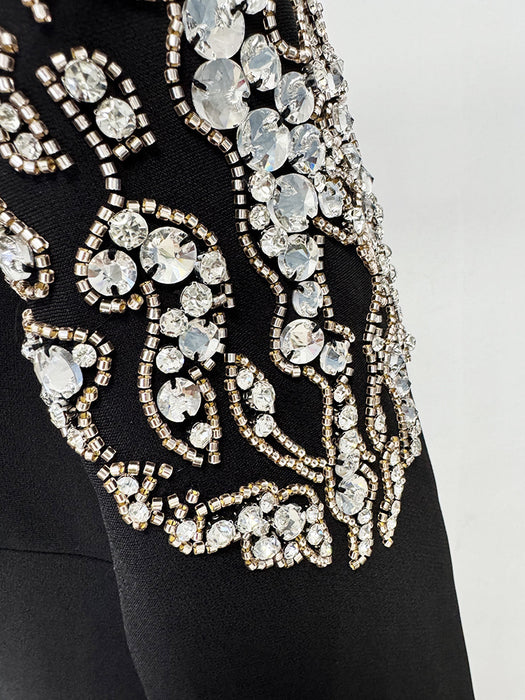 Close-up of a black garment with intricate gold and crystal embellishments on a light gray background