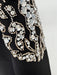 Close-up of a black garment with intricate gold and crystal embellishments on a light gray background
