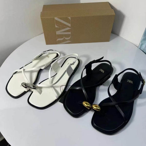 White and black sandals with gold accents on a white surface, Zara box in the background.