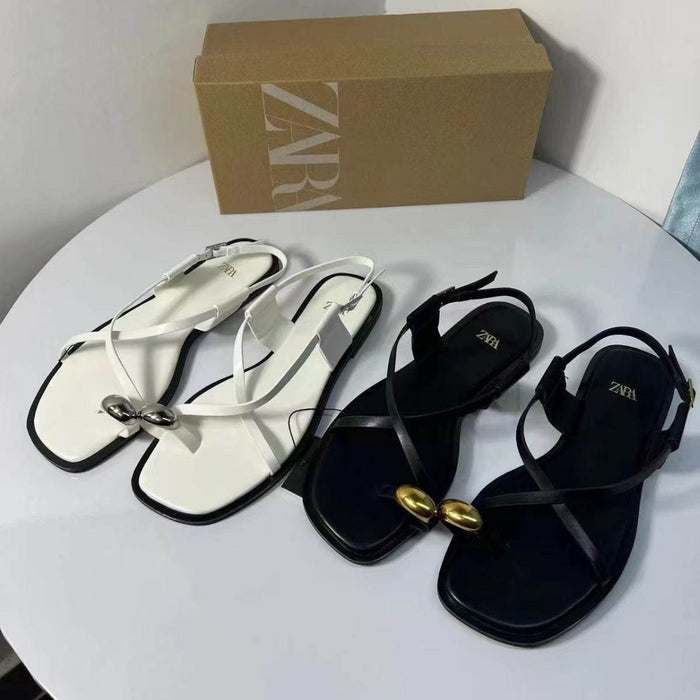 White and black sandals with gold accents on a white surface, Zara box in the background.