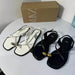 White and black sandals with gold accents on a white surface, Zara box in the background.