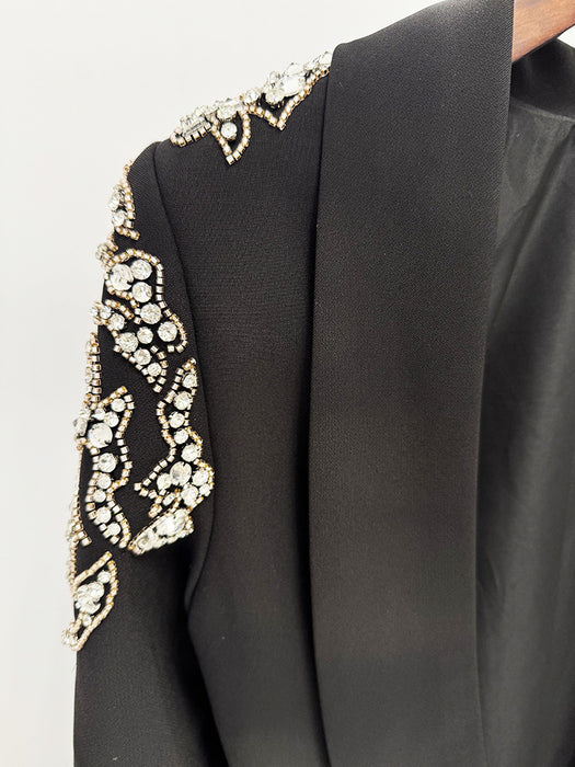 Black garment with gold and white embellishments on a plain background