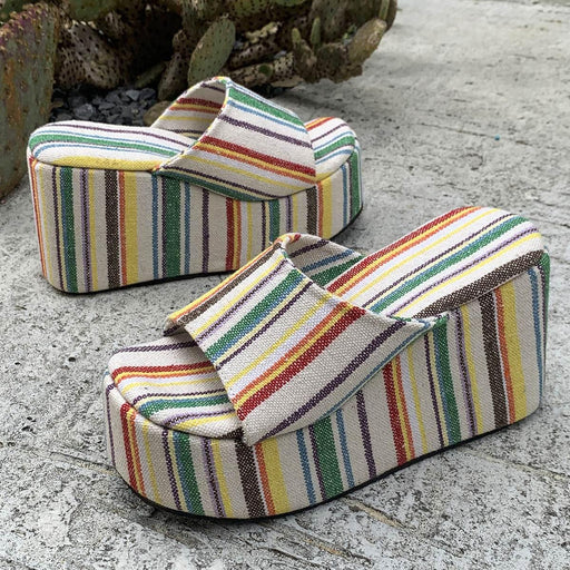 Two striped wedge sandals on a textured surface with a cactus in the background.