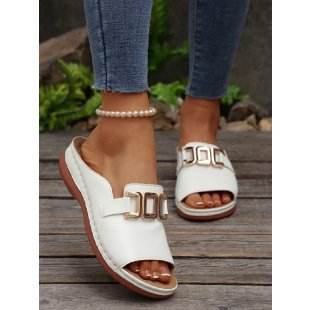 White sandals with gold buckles worn by a person on a wooden surface.