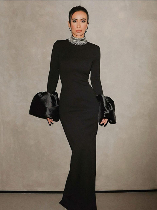 A woman wearing a black long-sleeve dress with a round neckline and a high waist, featuring a solid color with a zipper at the placket.
