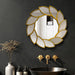 Decorative mirror with leaf-like design on a dark wall above a sink with gold fixtures.