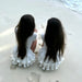 Two children in white dresses sitting on a sandy beach.